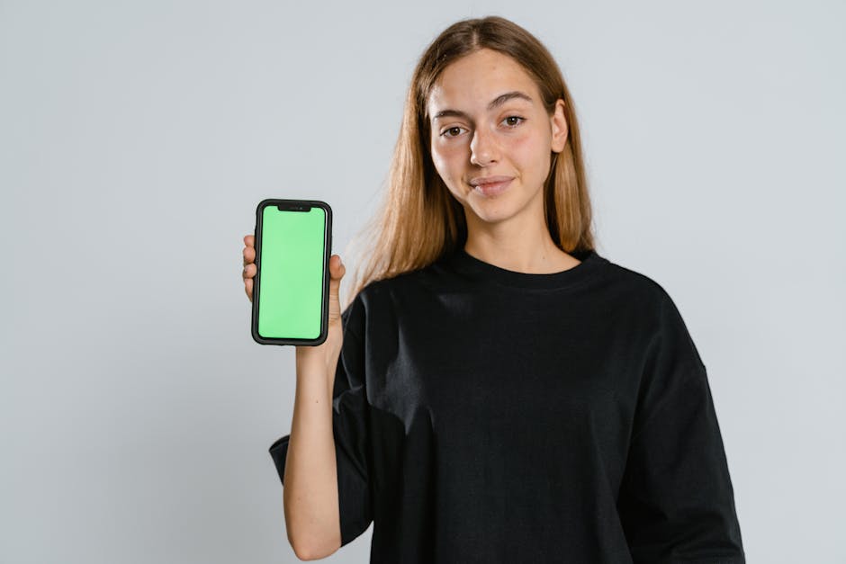 Young woman in black t-shirt showing a green screen smartphone in studio setting, ideal for mockup use